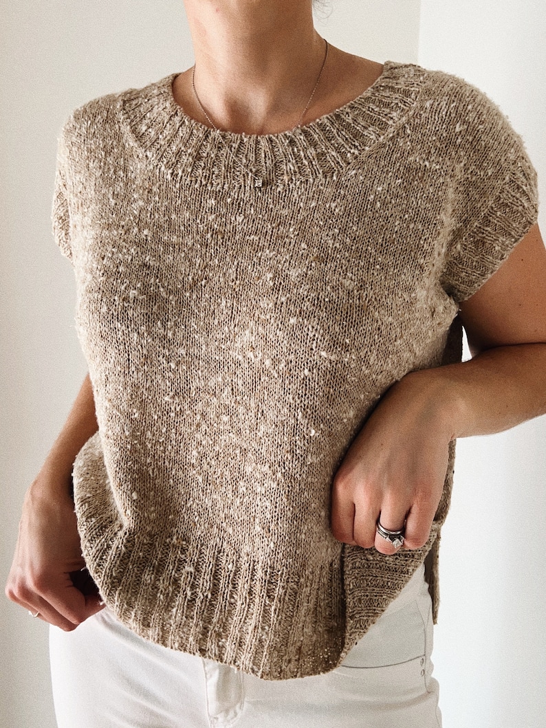 May include: A beige knitted top with short sleeves and a round neckline. The top has a speckled texture.