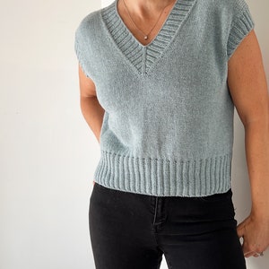 May include: A light blue sleeveless knitted sweater with a v-neck and a ribbed hem.
