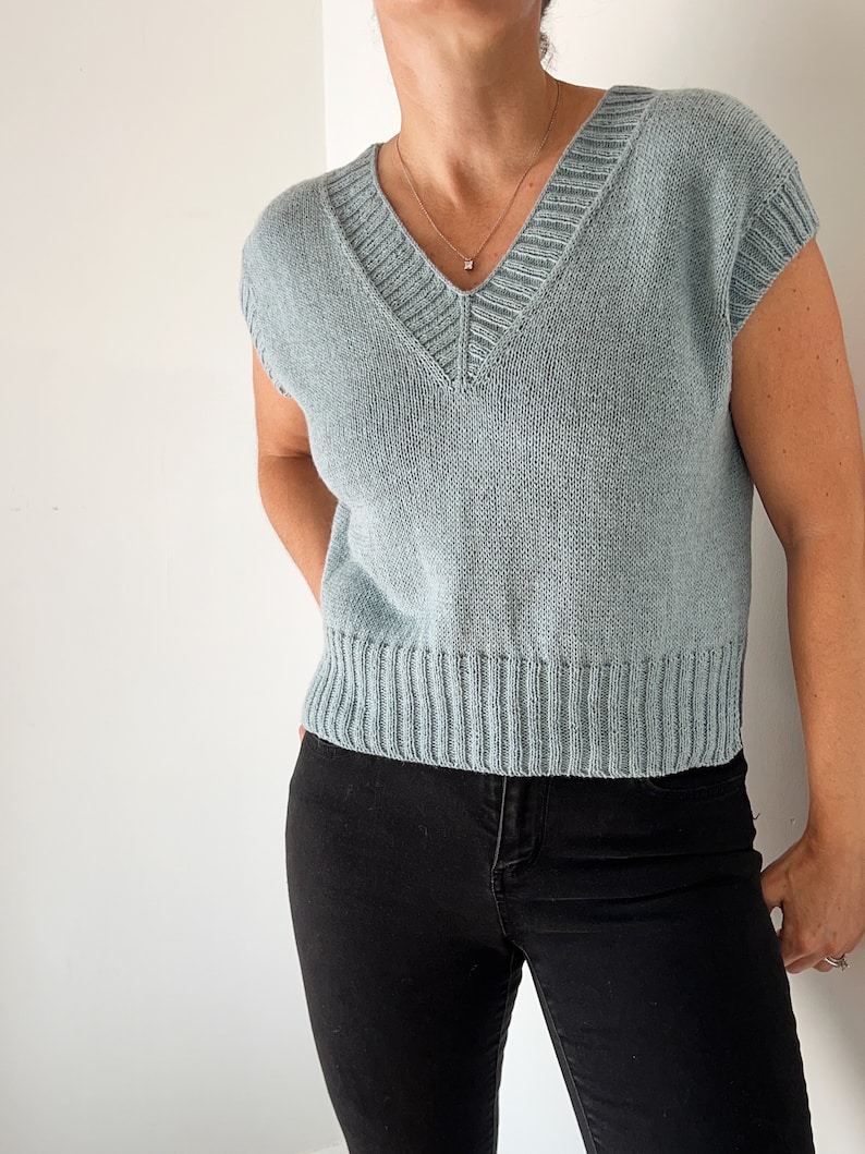 May include: A light blue sleeveless knitted sweater with a v-neck and a ribbed hem.