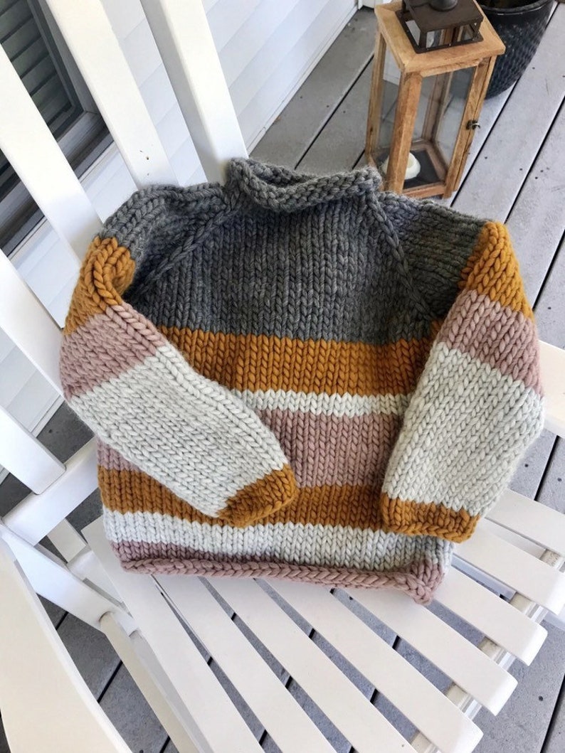 May include: A striped knit sweater with a grey, white, pink, and mustard yellow color scheme. The sweater has a turtleneck and long sleeves.