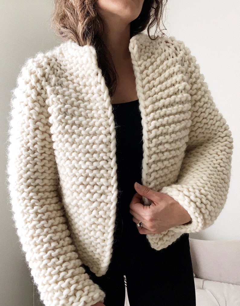 K&ouml;nnte beinhalten: Ein wei&szlig;er Strickcardigan mit leicht verk&uuml;rzter L&auml;nge und langen &Auml;rmeln. Der Cardigan hat einen schlichten, offenen V-Ausschnitt.