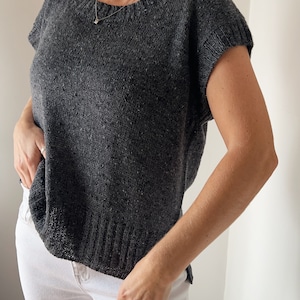 May include: A charcoal grey knitted top with short sleeves and a round neckline.