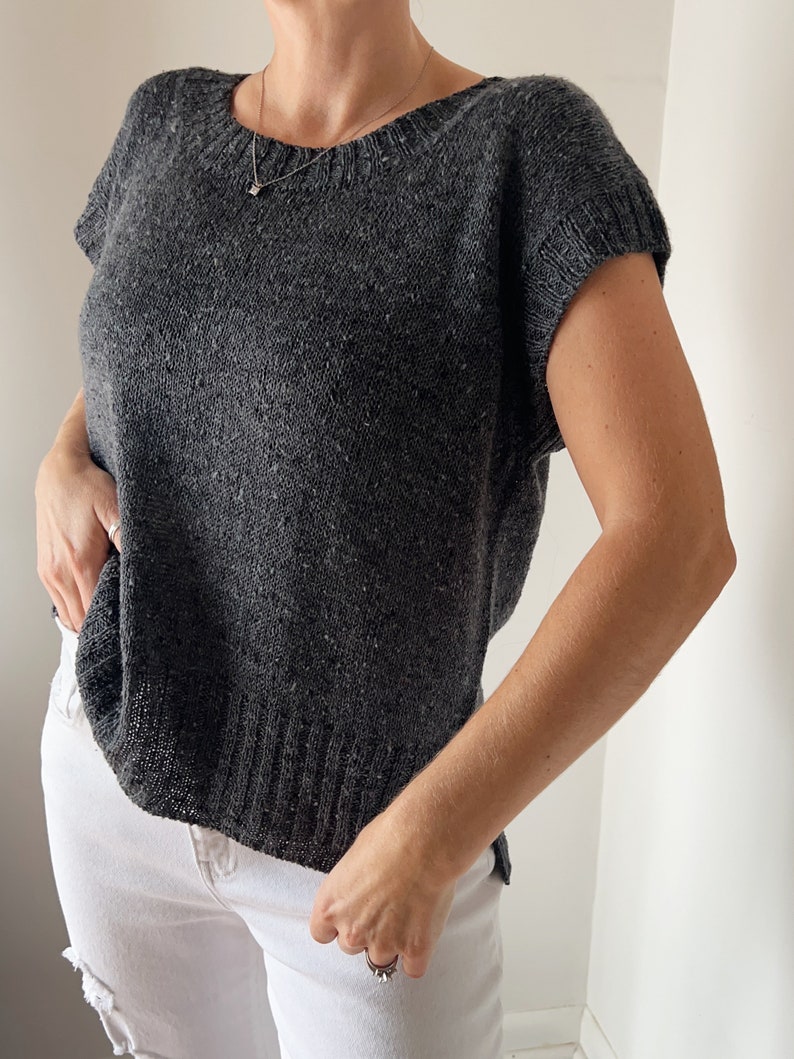 May include: A charcoal grey knitted top with short sleeves and a round neckline.