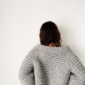 K&ouml;nnte beinhalten: Ein grauer Strickpullover mit lockerer Passform und langen &Auml;rmeln. Der Pullover ist aus dickem Garn gefertigt und hat einen leicht &uuml;berdimensionalen Look.