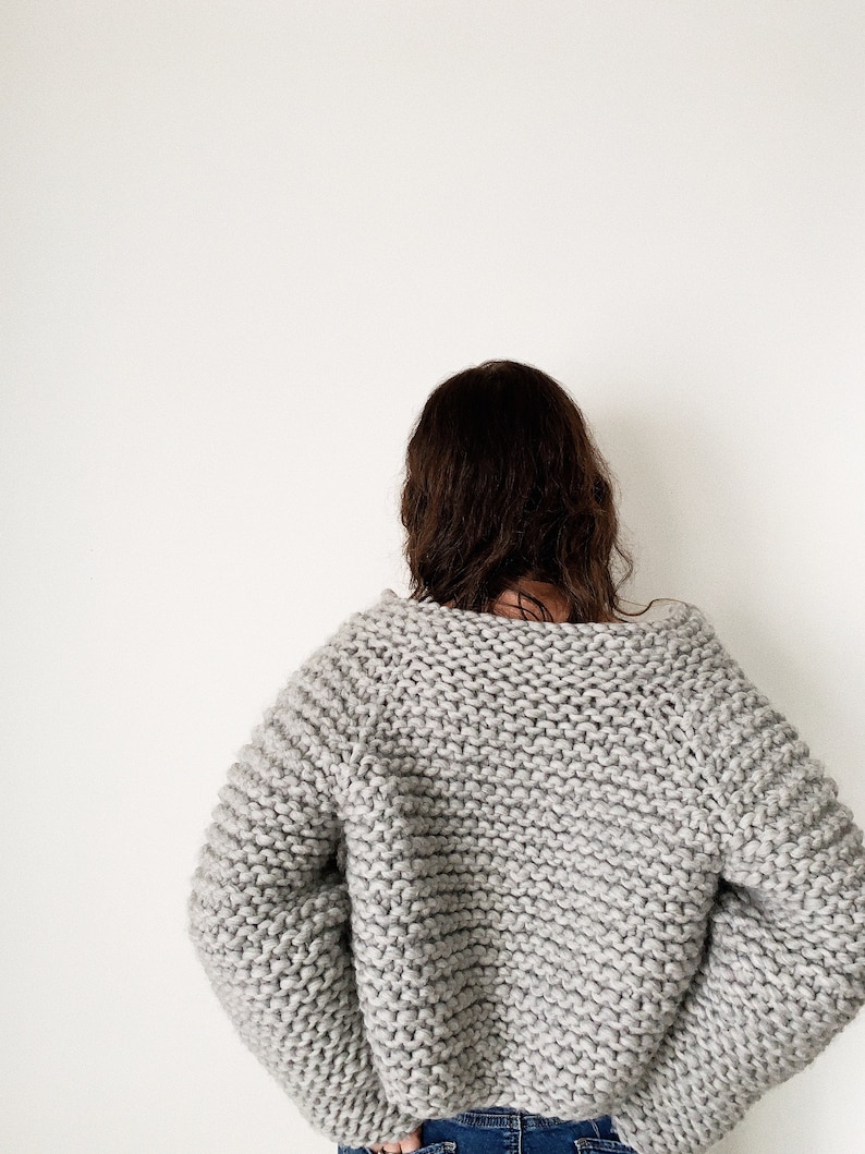 K&ouml;nnte beinhalten: Ein grauer Strickpullover mit lockerer Passform und langen &Auml;rmeln. Der Pullover ist aus dickem Garn gefertigt und hat einen leicht &uuml;berdimensionalen Look.