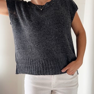 May include: A charcoal grey knitted top with short sleeves and a round neckline. The top has a ribbed hem and is made of a soft, textured yarn.