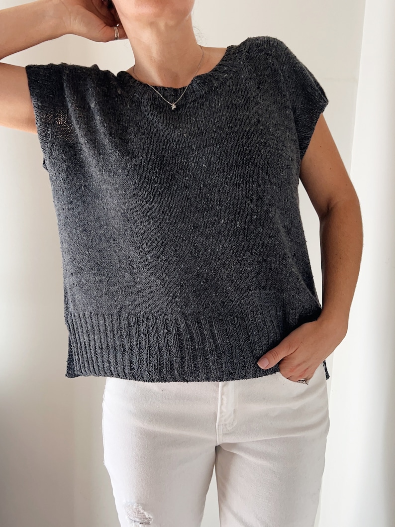 May include: A charcoal grey knitted top with short sleeves and a round neckline. The top has a ribbed hem and is made of a soft, textured yarn.