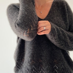 May include: A dark gray, fuzzy knit sweater with a V-neck and delicate lace detailing around the neckline and sleeves.