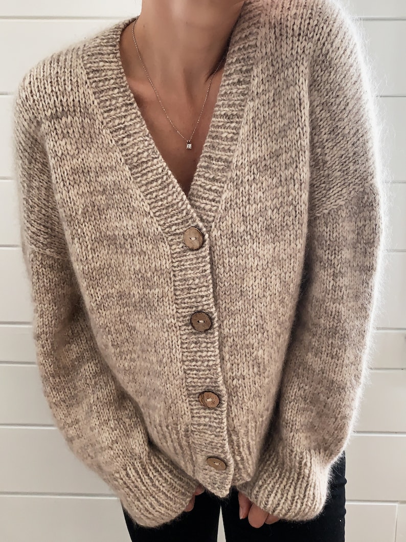 May include: A beige cardigan with a V-neck and wooden buttons. The cardigan is made of a soft, fuzzy material.