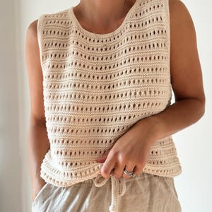 May include: A cream-colored crochet tank top with a loose fit and a drawstring at the bottom.