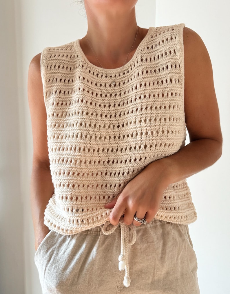 May include: A cream-colored crochet tank top with a loose fit and a drawstring at the bottom.