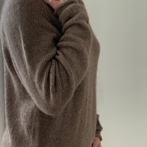 May include: A brown knitted jumper with long sleeves and a scoop neck.
