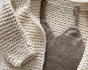 May include: A white chunky knit cardigan with a brown knit tank top underneath. Both garments are laid flat on a white surface.
