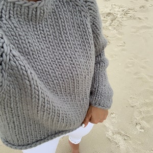May include: A gray chunky knit sweater with a high neckline and long sleeves. The sweater is made of a thick yarn and has a relaxed fit.