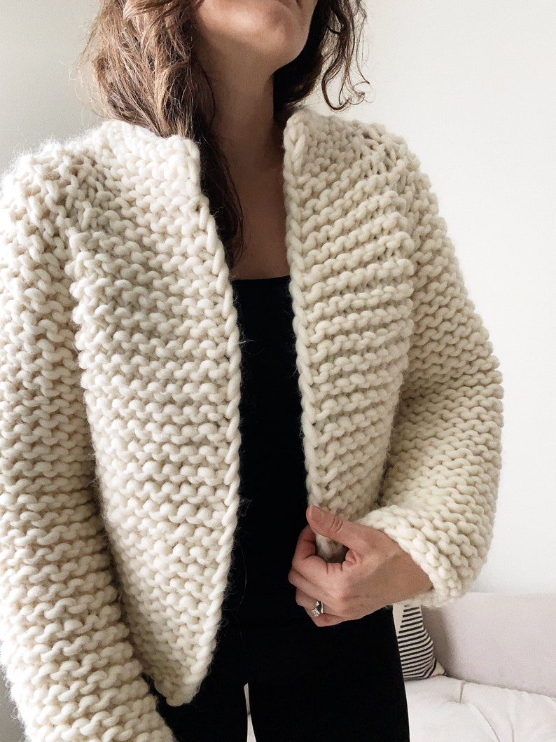 K&ouml;nnte beinhalten: Ein cremefarbener Strickcardigan mit leicht verk&uuml;rzter L&auml;nge und einem einfachen offenen Vorderteil.