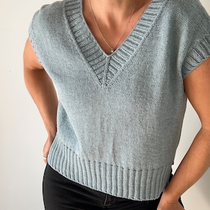 May include: A light blue knitted sleeveless top with a v-neck and a ribbed hem.