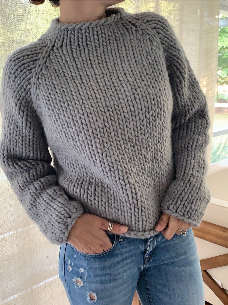 May include: A gray chunky knit sweater with a round neckline and long sleeves.