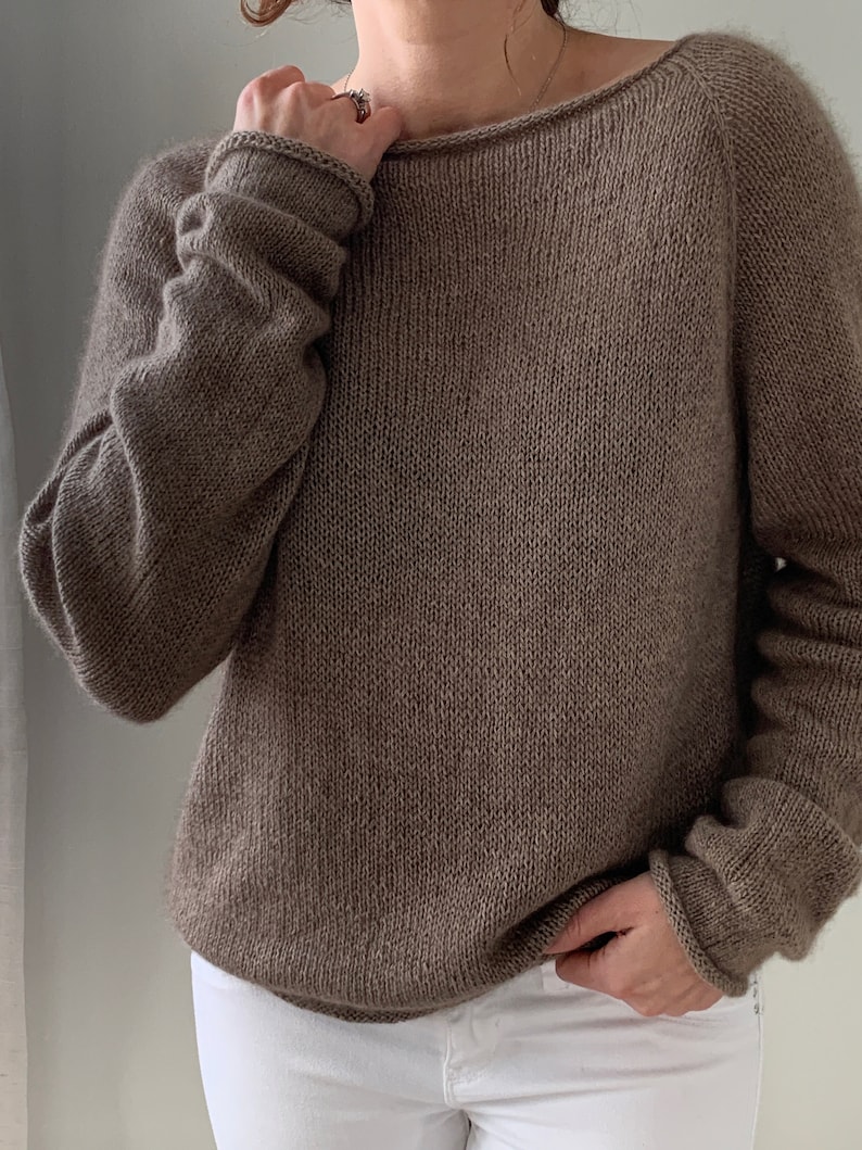 May include: A brown knitted jumper with a wide neckline and long sleeves.