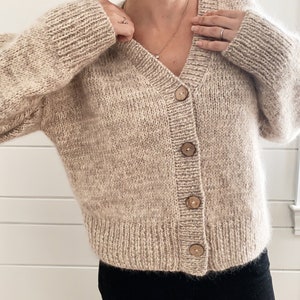 May include: A beige knitted cardigan with a v-neck and wooden buttons.