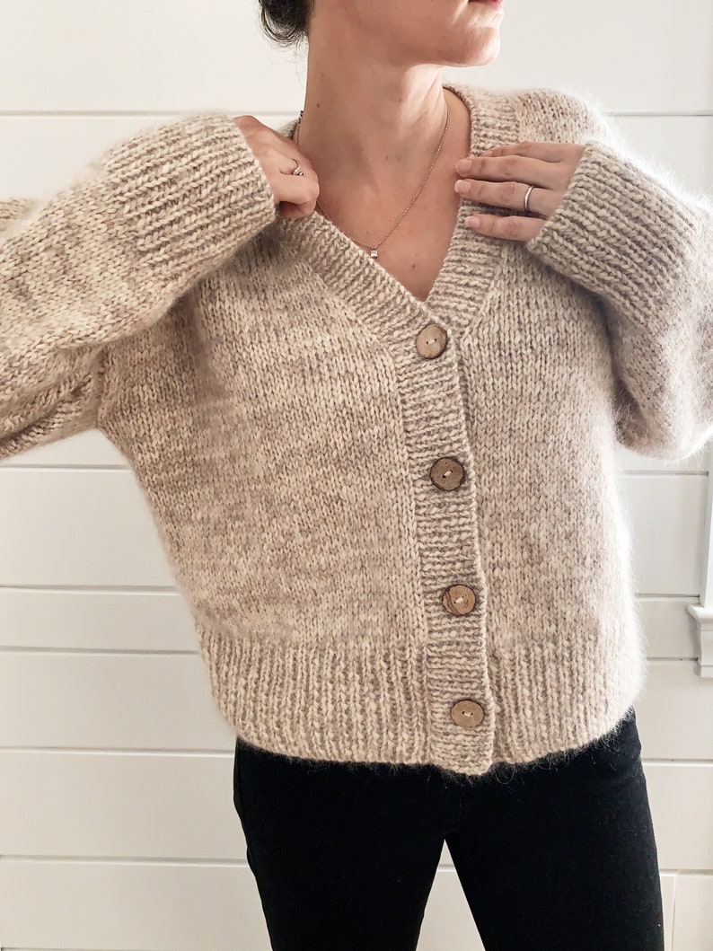 May include: A beige knitted cardigan with a v-neck and wooden buttons.