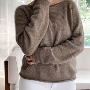 May include: A brown knitted jumper with a wide neckline and long sleeves.