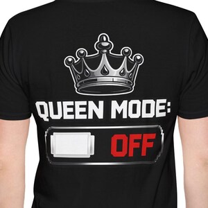 Może przedstawiać: Czarna koszulka z grafiką srebrnej korony nad napisem "QUEEN MODE: OFF" w kolorze białym i czerwonym. Projekt zawiera grafikę przypominającą baterię z białym prostokątem i słowem "OFF".