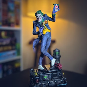 Puede incluir: Figura detallada del Joker, un supervillano de DC Comics, en una pose dinámica. La figura viste un traje morado, chaleco amarillo y pelo verde. Sostiene un bastón y una máscara de payaso, de pie sobre una base mecánica con una sonrisa amenazante.