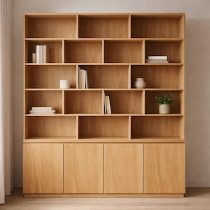 Könnte beinhalten: Ein großer, hellfarbiger Holzschrank mit mehreren Regalen und Schranktüren. Der Schrank ist mit Büchern, einer kleinen Topfpflanze und dekorativen Vasen gefüllt. Die Holzmaserung ist sichtbar, und das Design ist modern und minimalistisch.
