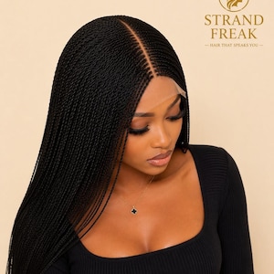 May include: A black braided lace front wig featuring long, thin, uniform micro-braids with a centre part. The hair is styled straight and falls past the shoulders. The brand logo STRAND FREAK with a crown icon is visible in the top right corner.