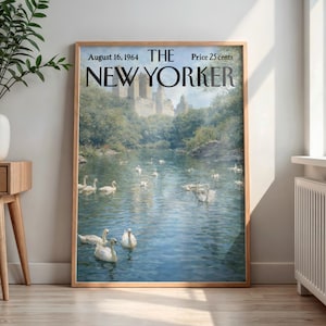 May include: A framed vintage New Yorker magazine cover from August 16, 1964, featuring a serene lake scene with swans and a castle in the background. The artwork is in a wooden frame, displayed indoors near a window and a side table.