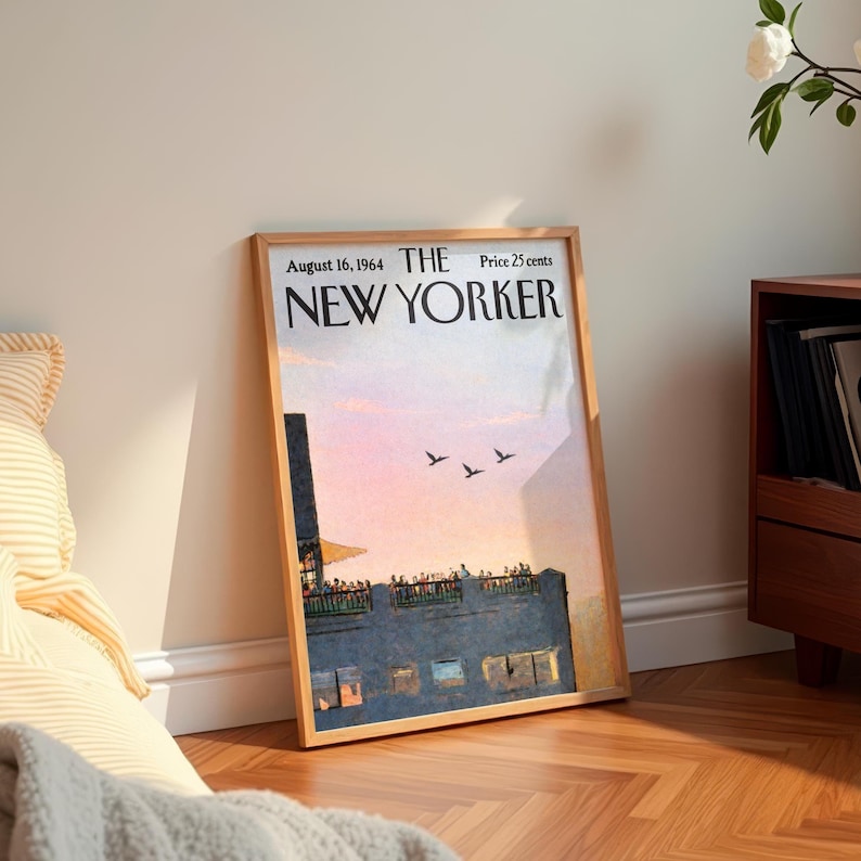 May include: A framed vintage New Yorker magazine cover from August 16, 1964, featuring a sunset scene over a city building with birds in flight. The cover is in a wooden frame, leaning against a wall.