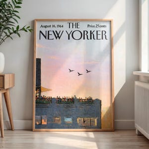 May include: A framed vintage New Yorker magazine cover from August 16, 1964, featuring a sunset scene with birds in flight. The artwork is in a wooden frame, displayed in a well-lit room with a side table and a vase.