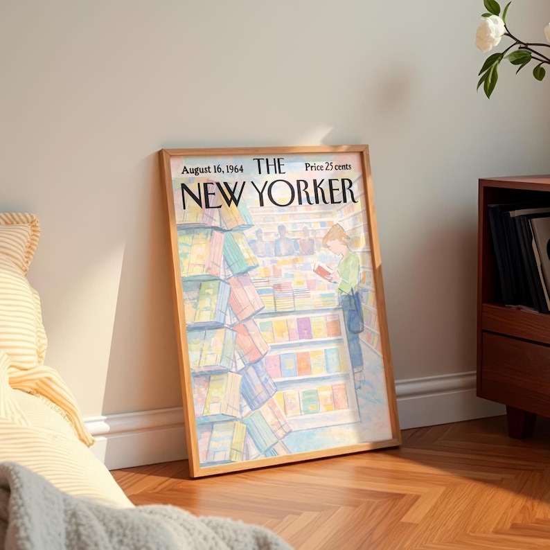 May include: A framed vintage New Yorker magazine cover from August 16, 1964, featuring a person reading in a bookstore. The cover art depicts colorful books and shelves. The frame is a light brown color.