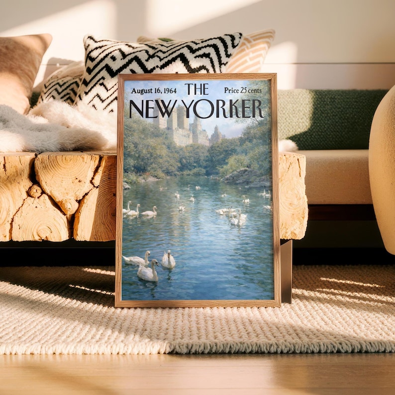 May include: A framed vintage New Yorker magazine cover from August 16, 1964, featuring a serene lake scene with swans. The cover art is set in a wooden frame, resting on a neutral-toned rug. The magazine's title and price are visible.