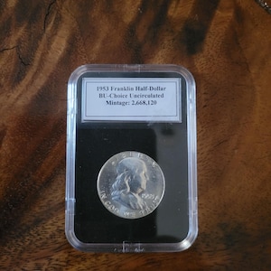 May include: A white ceramic mug with a black handle and the text "But First, Coffee" in a black, bold font. The mug is on a white surface.