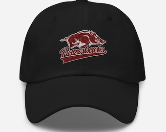 May include: Black baseball cap featuring a red Razorbacks logo. The logo includes a stylized image of a Razorback hog and the word "Razorbacks" in a matching red font. The cap has a curved brim and an adjustable strap.