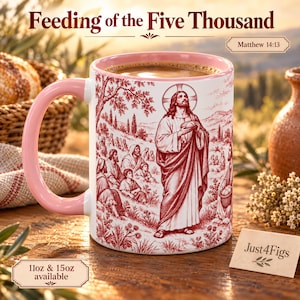 May include: A white ceramic mug with a pink handle and interior, featuring a red monochromatic illustration of the Feeding of the Five Thousand. The design depicts a central figure holding bread before a crowd in a landscape setting.