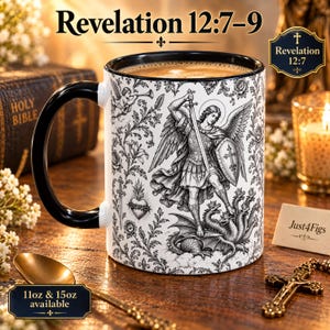 May include: A white ceramic mug with a black handle and rim, featuring a detailed black and white illustration of an angel with a sword and shield defeating a multi-headed dragon, surrounded by floral patterns and the text Revelation 12:7-9.