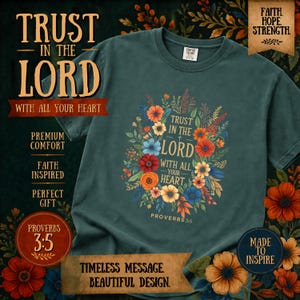 以下が含まれることがあります： 花柄のデザインと「Trust in the Lord with all your heart」の文字が入った濃いティール色のTシャツ。デザインにはカラフルな花と聖書の箴言3:5が含まれています。シャツには「Premium Comfort」、「Faith Inspired」、「Perfect Gift」の文字も入っています。
