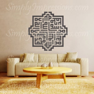May include: A black and white geometric design with Arabic calligraphy in a square shape. The design is on a beige wall above a light brown couch with two pillows.