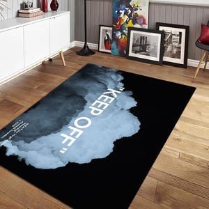 May include: A rectangular black rug featuring a cloud design in blue and white, with the words "KEEP OFF" in white. The rug's design is modern and minimalist, suitable for a living room or bedroom. The rug is made of a soft material.