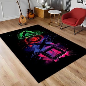 Könnte beinhalten: Schwarzer rechteckiger Teppich mit einem farbenfrohen Spritzdesign von Videospiel-Controller-Symbolen. Die Symbole sind in Grün, Rot, Blau und Pink gehalten. Der Teppich liegt auf einem Holzboden.