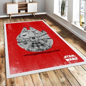 Puede incluir: Alfombra rectangular roja con una ilustración detallada de la nave espacial Halcón Milenario. La alfombra tiene un borde blanco y el logotipo de Star Wars. La alfombra está sobre un suelo de madera. Mide aproximadamente 180 cm x 120 cm.