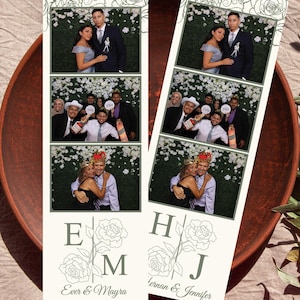 May include: Two photo booth strips with three photos each, featuring a couple and a group of people. The strips have a floral design at the top and bottom, with the initials "E M" and "H J" and names below. The photos are in a vertical format.