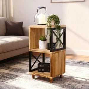 May include: A two-tiered wooden side table with a natural finish and black metal accents. The table features a decorative lantern, potted plants, and decorative boxes. The table is 24 inches tall and 18 inches wide.