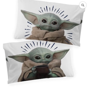 May include: Two white pillowcases featuring a green alien character with large ears and dark eyes. The character is wearing a brown robe and holding a dark brown cup. Blue lines radiate from the character's head.