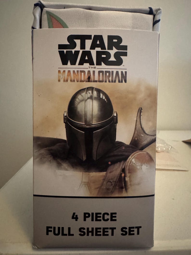 May include: A box for a Star Wars: The Mandalorian full sheet set. The box features the Star Wars logo and the Mandalorian's helmet. The text "4 Piece Full Sheet Set" is printed on the bottom of the box.