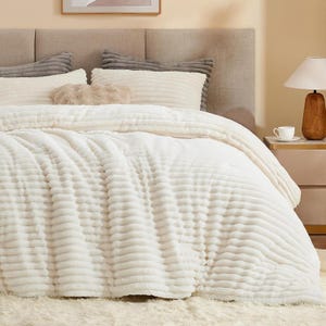 May include: A cream-colored bedding set featuring a textured, ribbed pattern on the duvet cover and matching rectangular pillows. The set includes a plush, fuzzy throw pillow in a light tan shade, all arranged on a bed with a gray headboard.
