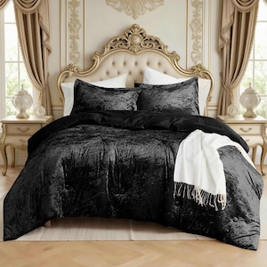 May include: A black velvet comforter set on a bed with a gold headboard. The set includes a comforter, two pillow shams, and a white throw blanket with fringe. The bedding is arranged in a bedroom with gold curtains and side tables.