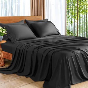 May include: A bed is made with black sheets and pillowcases. The bed is on a wooden frame. The sheets are draped over the bed. The room has a window with bamboo plants outside.